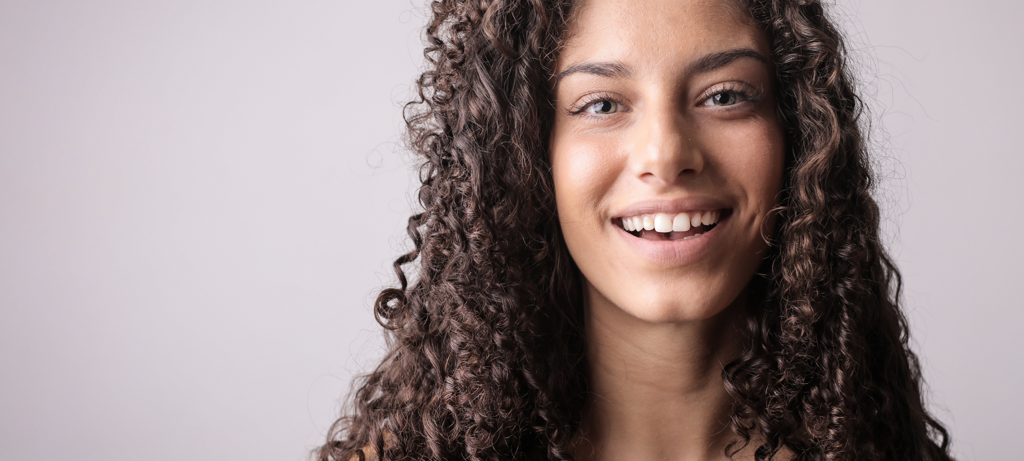 Smiling curly-haired brunette woman close up with neutral background